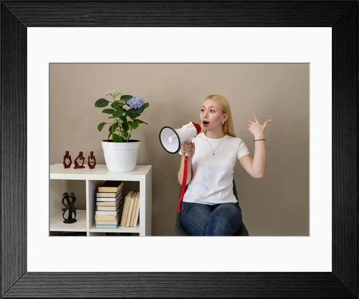 Framed Print : Blonde woman in casual white t-shirt and jeans gestures passionately while speaking into a red-and-white megaphone Framed Print : Blonde woman in casual white t-shirt and jeans gestures passionately while speaking into a red-and-white megaphone