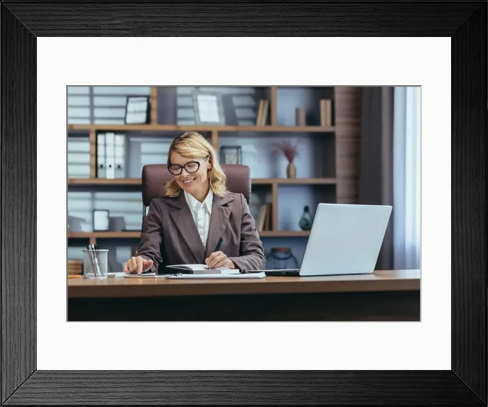 Framed Print : Elegant senior woman in business attire smiles while working at her laptop in a well-appointed home office setup
