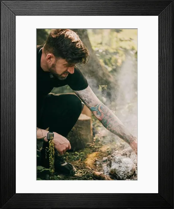 Framed Print : A man with tattoos on his arm is sitting on the ground next to a fire Framed Print : A man with tattoos on his arm is sitting on the ground next to a fire