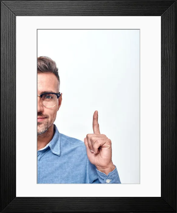 Framed Print : Look here Half face portrait of a smiling man with a stubble in eyewear gesturing and looking at camera Framed Print : Look here Half face portrait of a smiling man with a stubble in eyewear gesturing and looking at camera
