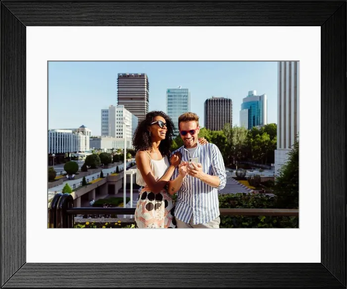 Framed Print : Beautiful black Woman and handsome Caucasian man using smartphone while standing on background of modern city