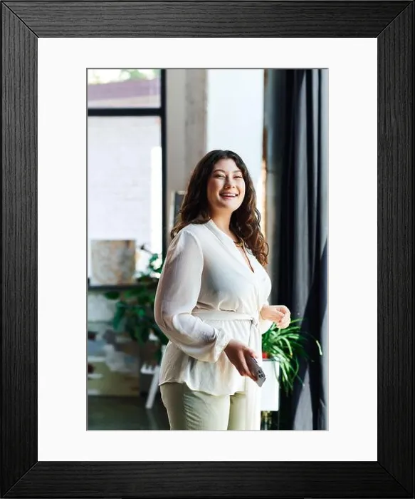Framed Print : A young beautiful plus size woman stands happily in her stylish office, surrounded by plants Framed Print : A young beautiful plus size woman stands happily in her stylish office, surrounded by plants