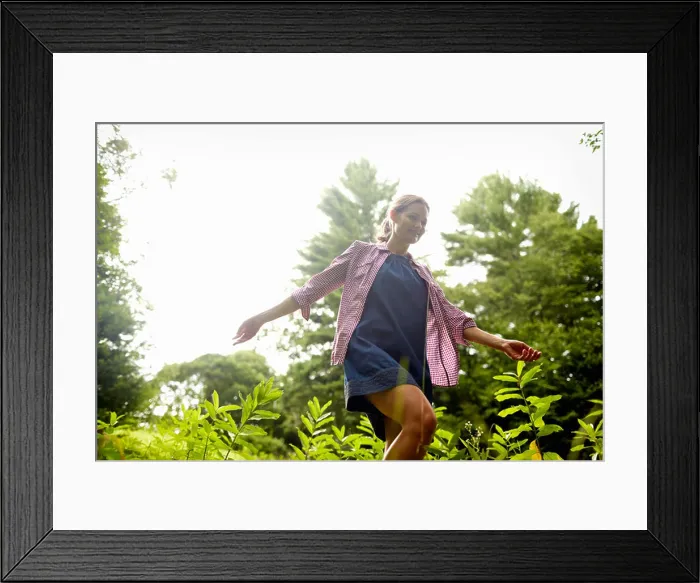 Framed Print : A woman walking through the undergrowth in woodland, with her arms brushing the tops of the wild plants