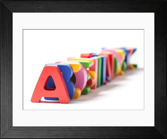 Framed Print : Wooden alphabet letters painted in different colors stacked one behind the other on white
