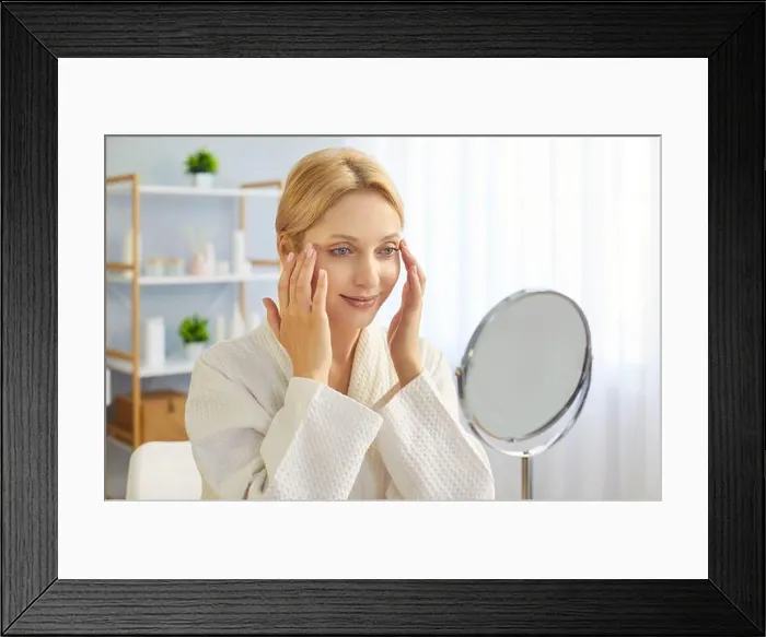 Framed Print : Young blonde woman in bathrobe gently touching her face skin