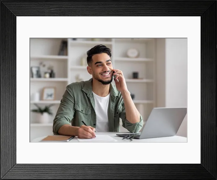 Framed Print : Smiling handsome millennial islamic guy manager with beard speaks by phone at workplace with laptop in home Framed Print : Smiling handsome millennial islamic guy manager with beard speaks by phone at workplace with laptop in home