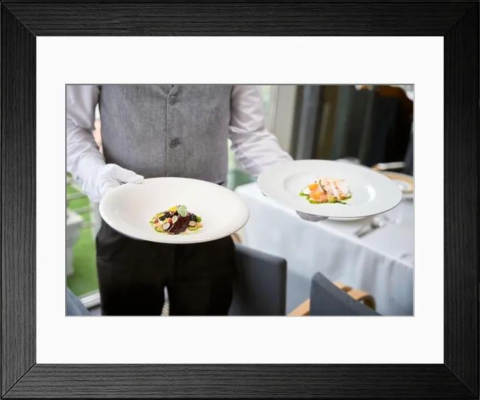 Framed Print : Cropped photo of male waiter in uniform carrying two plates of salads in a restaurant Framed Print : Cropped photo of male waiter in uniform carrying two plates of salads in a restaurant
