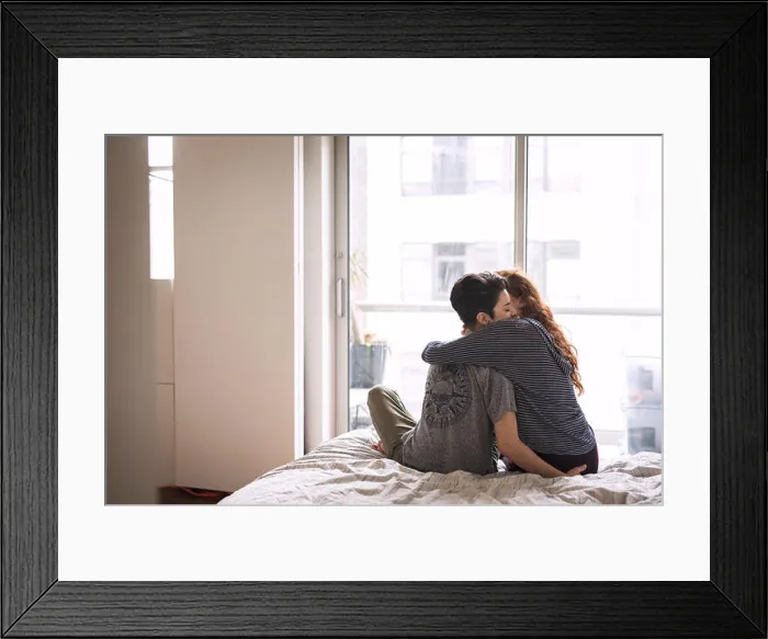 Framed Print : Romantic lesbians embracing while sitting on bed at home Framed Print : Romantic lesbians embracing while sitting on bed at home