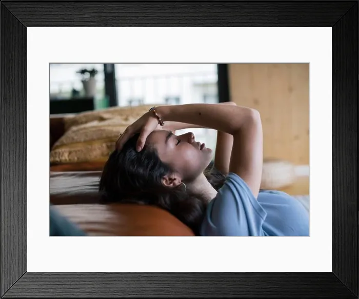 Framed Print : Side view of depressed woman with hand in hair reclining on sofa at home Framed Print : Side view of depressed woman with hand in hair reclining on sofa at home