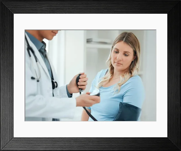 Framed Print : a doctor using a blood pressure gauge during a checkup with his pregnant patient