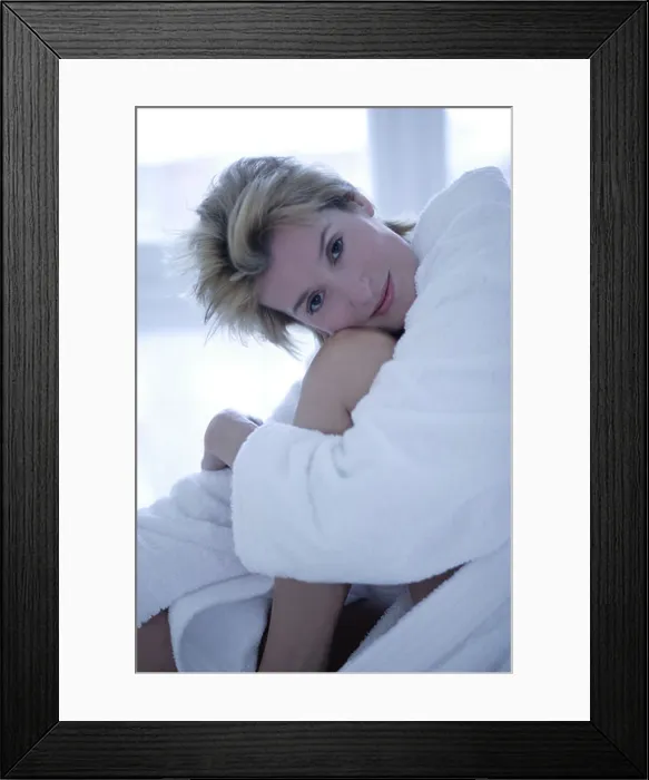 Framed Print : A woman sitting on the edge of a bed hugging her knees, close up
