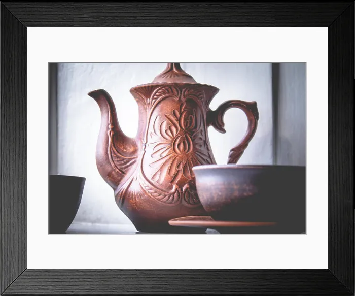 Framed Print : A teapot and a cup of clay are standing near the window. Close-up Framed Print : A teapot and a cup of clay are standing near the window. Close-up