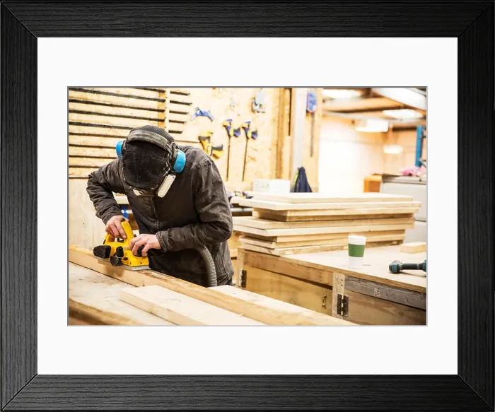 Framed Print : Man wearing ear protectors, protective goggles and dust mask standing in a warehouse, sanding planks of recycled wood Framed Print : Man wearing ear protectors, protective goggles and dust mask standing in a warehouse, sanding planks of recycled wood