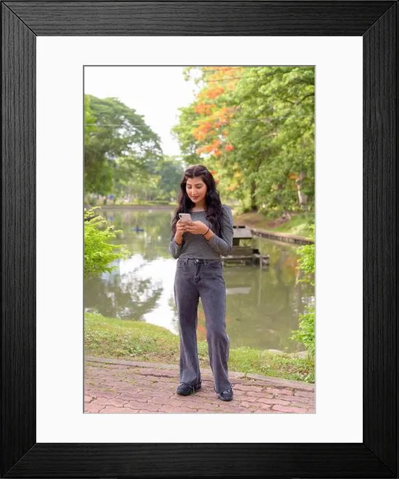 Framed Print : Full body shot of young beautiful Indian woman using phone at the park outdoors Framed Print : Full body shot of young beautiful Indian woman using phone at the park outdoors