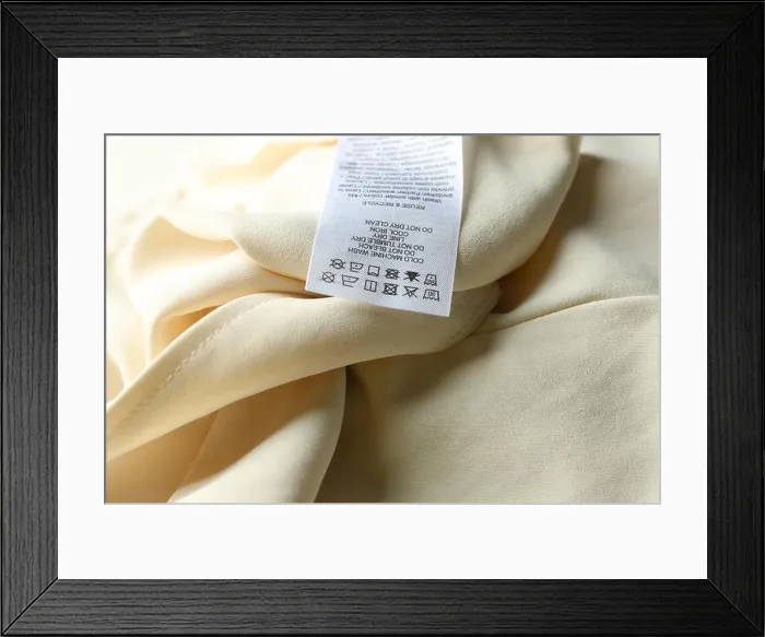 Framed Print : Clothing label with care instructions on beige garment, closeup Framed Print : Clothing label with care instructions on beige garment, closeup