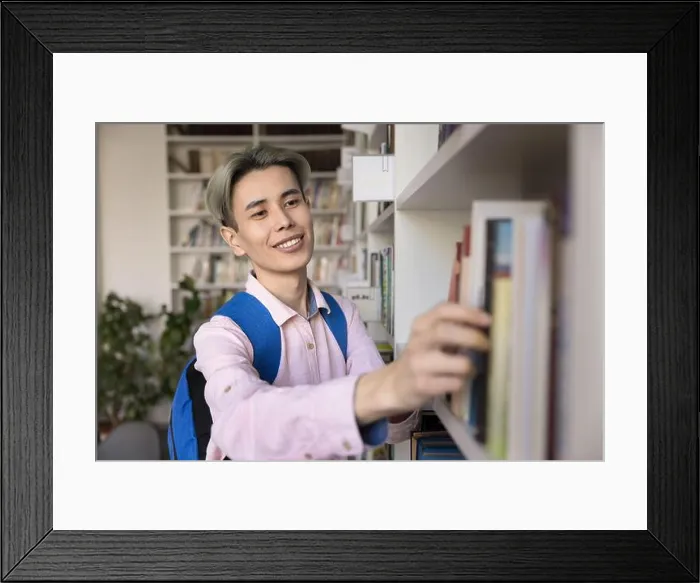 Framed Print : Happy Asian teen student guy choosing literature in university library Framed Print : Happy Asian teen student guy choosing literature in university library