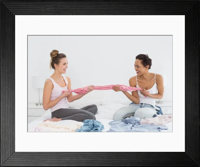 Framed Print : Pretty friends jokingly fighting over clothes on bed Framed Print : Pretty friends jokingly fighting over clothes on bed