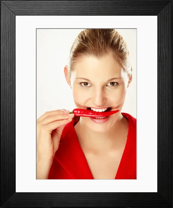 Framed Print : Young woman holding chilies between teeth, close-up, portrait Framed Print : Young woman holding chilies between teeth, close-up, portrait