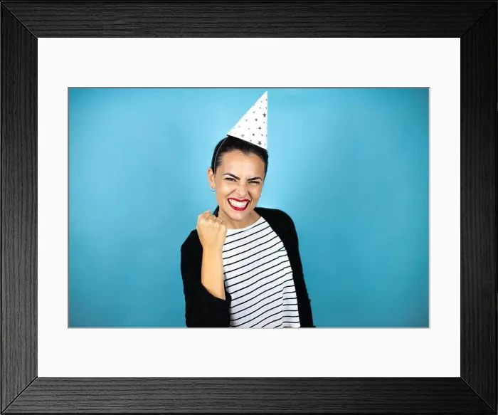 Framed Print : Young beautiful woman wearing a birthday hat over insolated blue background angry and mad raising fist frustrated Framed Print : Young beautiful woman wearing a birthday hat over insolated blue background angry and mad raising fist frustrated