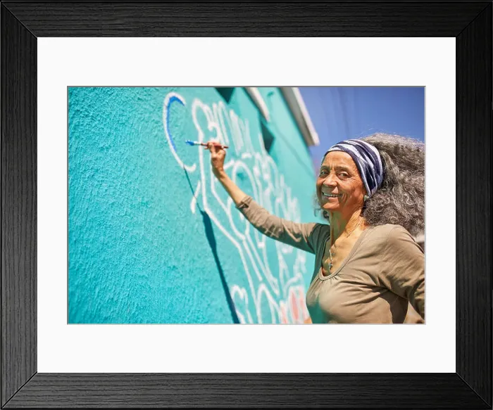 Framed Print : Portrait happy senior female volunteer painting on sunny wall Framed Print : Portrait happy senior female volunteer painting on sunny wall