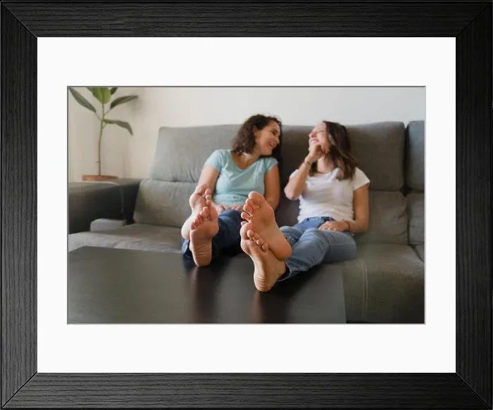 Framed Print : Girls in a couch with feet in a table laughing Framed Print : Girls in a couch with feet in a table laughing