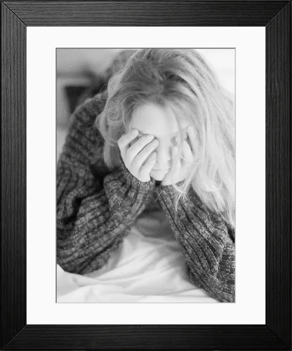 Framed Print : Woman lying on bed, leaning on elbows, hands over face, black and white