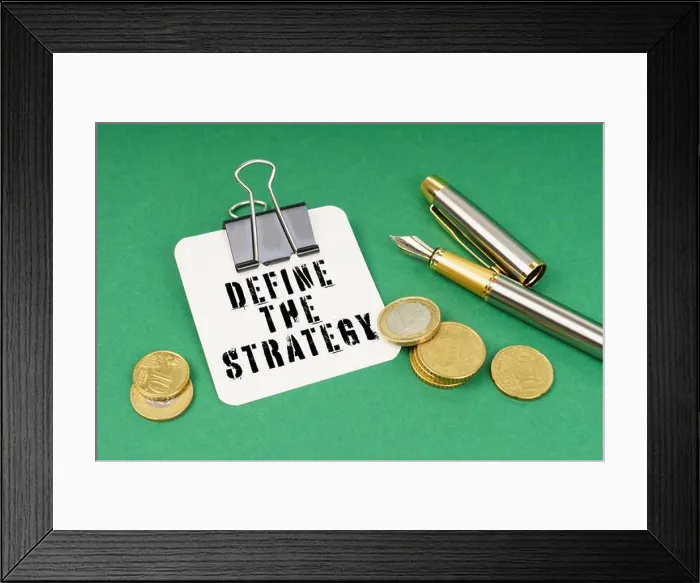 Framed Print : Business and finance concept. On a green surface, a pen, coins and a notepad with the inscription - Define The Strategy Framed Print : Business and finance concept. On a green surface, a pen, coins and a notepad with the inscription - Define The Strategy