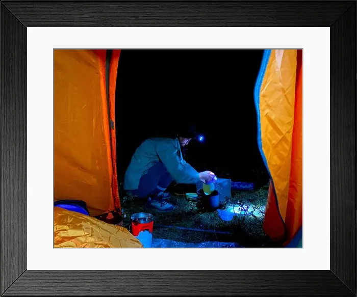 Framed Print : View from a tourist tent at night on a traveler girl with a lantern cooking food in a saucepan. Framed Print : View from a tourist tent at night on a traveler girl with a lantern cooking food in a saucepan.