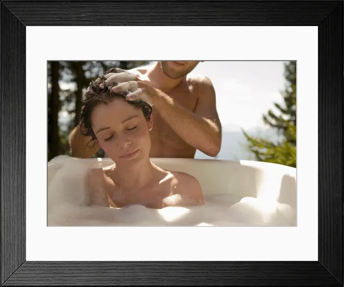 Framed Print : Young woman lying in bathtub, young man washing hair Framed Print : Young woman lying in bathtub, young man washing hair