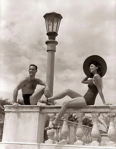 1930s 1940s MAN WOMAN SUN HAT COUPLE BATHING SUITS SITTING ON BALUSTRADE WALL TROPICAL VACATION HOTEL MIAMI BEACH FLORIDA USA - s2169 HAR001 HARS