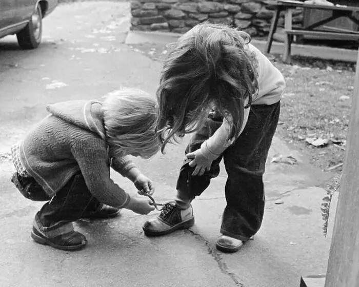 Framed Print : 1970s 1970s BLOND BOY BENDING OVER HELPING GIRL TIE HER SHOE