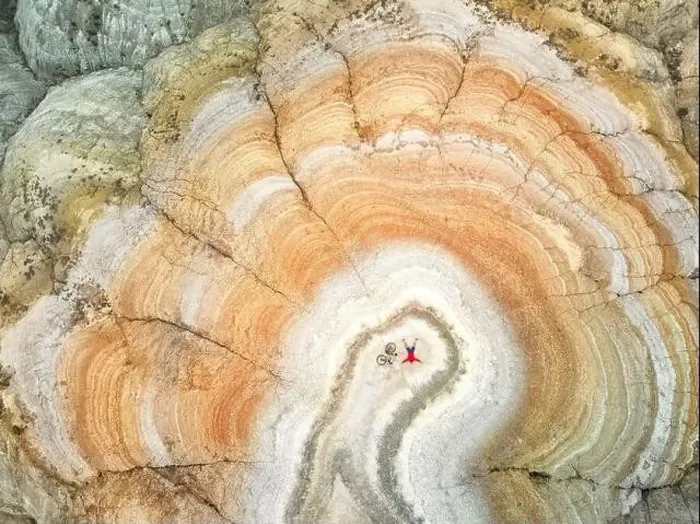 Framed Print : Aerial drone shot of man lying with his bicycle on the top of surreal striped red and white desert mountain Framed Print : Aerial drone shot of man lying with his bicycle on the top of surreal striped red and white desert mountain