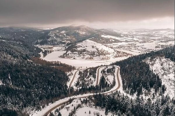 Aerial drone view over the winter mountains with mountain road serpentine, river and forest. Landscape photography