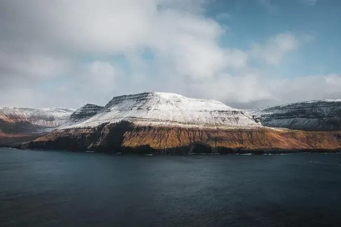 Framed Print : Aerial helicopter shot of snow-covered mountains at the shore of the Faroe Islands with low-hanging clouds during cold Framed Print : Aerial helicopter shot of snow-covered mountains at the shore of the Faroe Islands with low-hanging clouds during cold