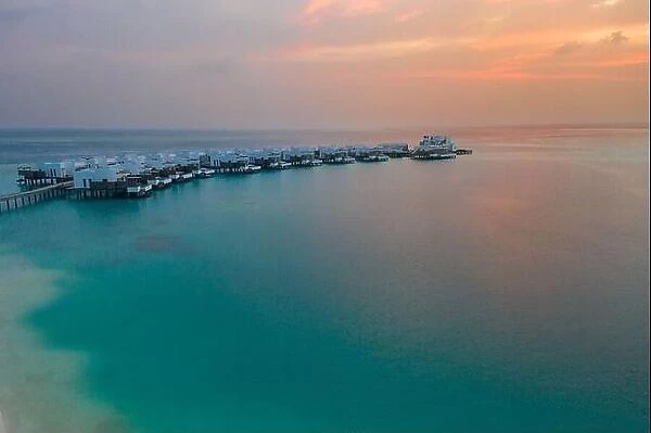 Aerial Maldives island sunset. Water bungalows resort at islands beach. Aerial Maldives. Beautiful sunset landscape, luxury resort and colorful sky