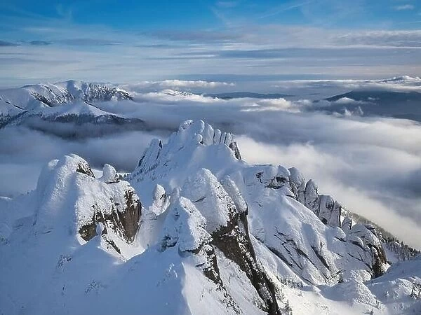 Aerial view of distant mountain peaks above clouds in clear sunny blue sky