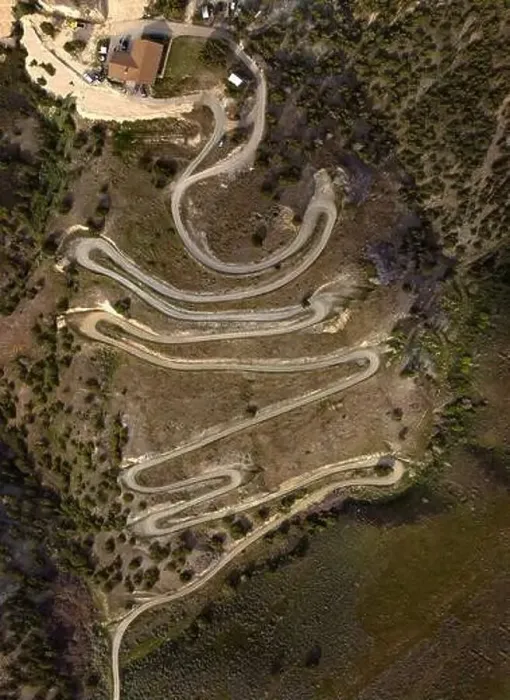 Framed Print : Aerial view from a drone flying above a winding curved dirt road on mountainside