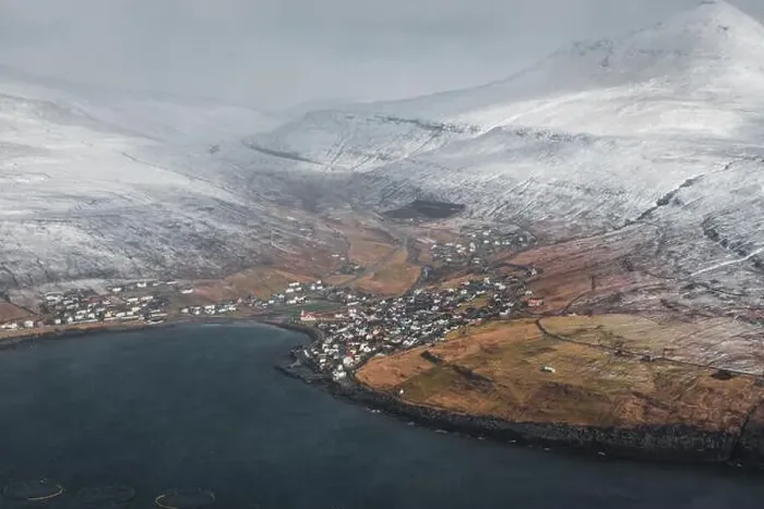 Framed Print : Aerial view of a Faroese village within a calm bay surrounded by snow-covered mountains as seen from a helicopter in Framed Print : Aerial view of a Faroese village within a calm bay surrounded by snow-covered mountains as seen from a helicopter in