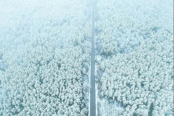 Aerial view of highway road through snow forest landscape in winter. Top view of highway motorway freeway from high attitude. Trip and travel concept