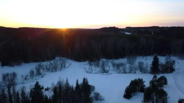 Framed Print : Aerial view of a snowmobile driving along pine tree forest. Clip. Sunset sky and rural snow covered road