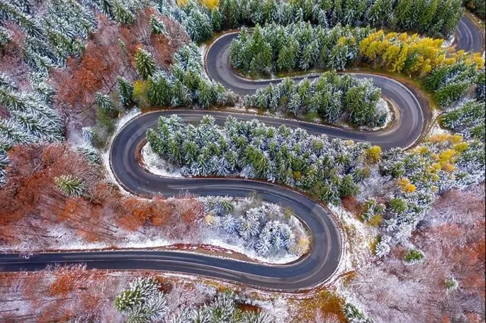 Framed Print : Aerial view of a winding mountain road passing through a fir trees forest. Winter with snow