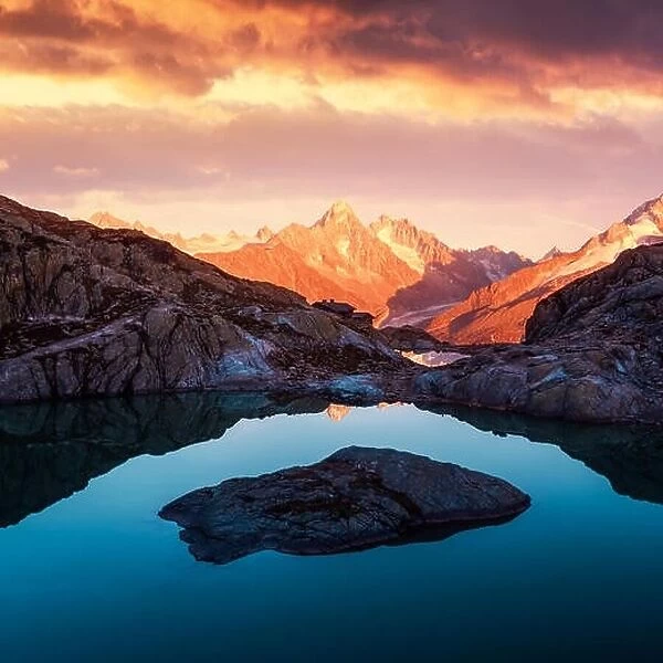 Alpine mountain landscape with lake and peaks covered by snow on sunset time