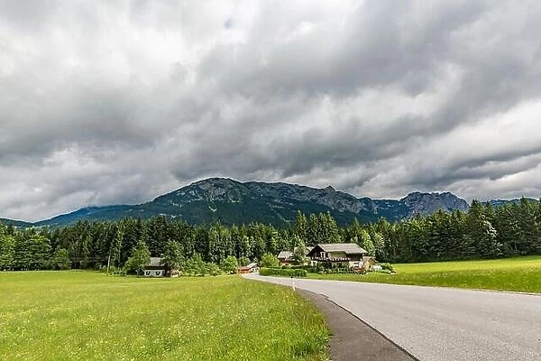 Alps in Austria. Wooden house before mountains green field and road through green pine forest