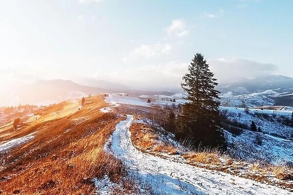 Amazing view of mountains range and meadows of the countryside in spring time. Clear sky and snowy road glowing with bright sunset light