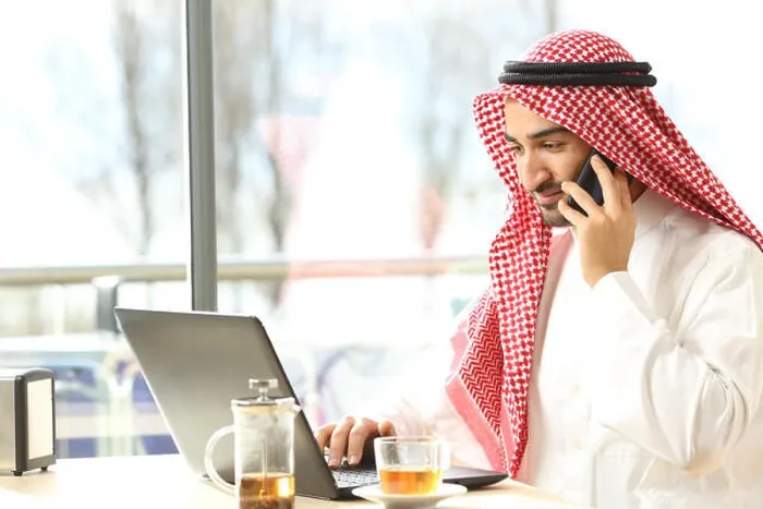 Framed Print : Arab man working on the phone and a laptop in a coffee shop with a window in the background Framed Print : Arab man working on the phone and a laptop in a coffee shop with a window in the background