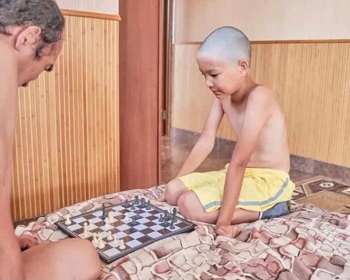 Framed Print : Asian tanned boy with a haircut bald, in yellow shorts, playing chess with an adult on the bed at home Framed Print : Asian tanned boy with a haircut bald, in yellow shorts, playing chess with an adult on the bed at home