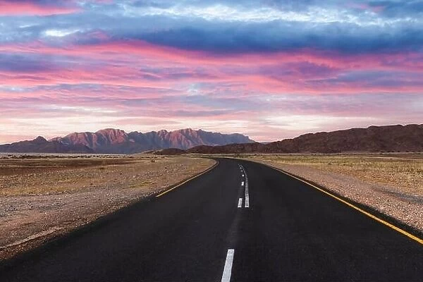 Asphalt road through desert savanna in of Namib at Namib-Naukluft National Park in Namibia, Africa. Highway and sunset sky