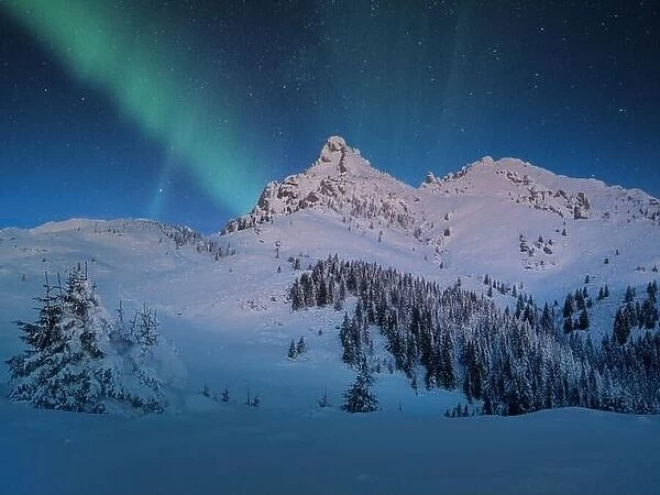 Aurora Borealis appear over a snow covered mountain in winter landscape. Northern lights mountain landscape