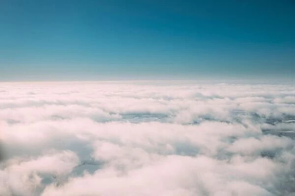 Beautiful Aerial View Of Sunny Clear Sky Over White Fluffy Clouds From Height Flight Of Plane. Bright White And Blue Colors Of Sunny Sky
