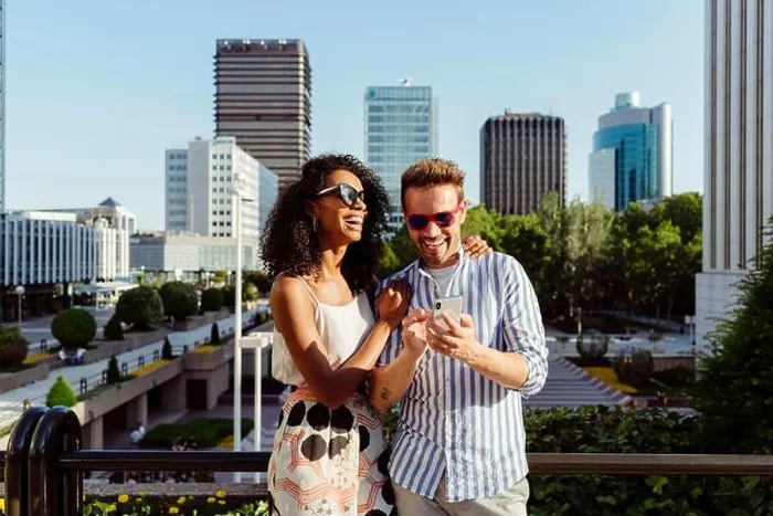 Framed Print : Beautiful black Woman and handsome Caucasian man using smartphone while standing on background of modern city